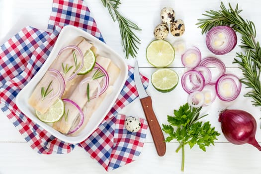 Sliced herring fillets, cut onion and lime on white plate. Checkered napkin. On wooden table.