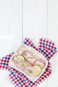 Sliced herring fillets, cut onion and lime on white plate. Checkered napkin. On wooden table.