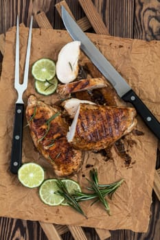 Sliced grilled chicken filet with herbs  on a paper on wooden background. Rosemary and sliced lime on a dark groundwork.
