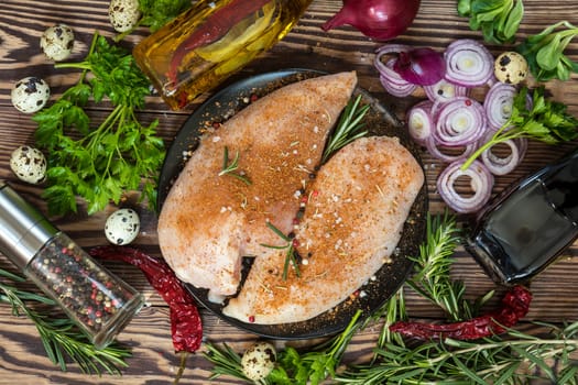 Raw uncooked chicken fillet on a cutting table with ingredients for cooking, on black plate. Top view. Toned.