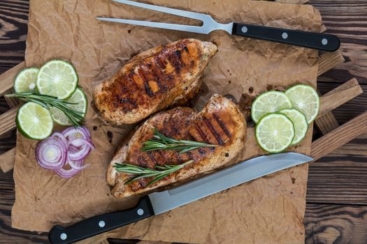 Grilled chicken filet with herbs  on a paper on wooden background. Rosemary and sliced lime on a dark groundwork.