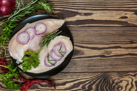 Raw uncooked chicken fillet on a cutting table with ingredients for cooking, on black plate. Top view. Toned. Copy space.