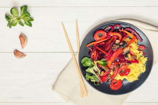 Healthy vegetarian diet concept. Rice and steamed vegetables, lamb's lettuce feldsalat on a black plate, chopsticks, napkin, garlic. White wooden table.