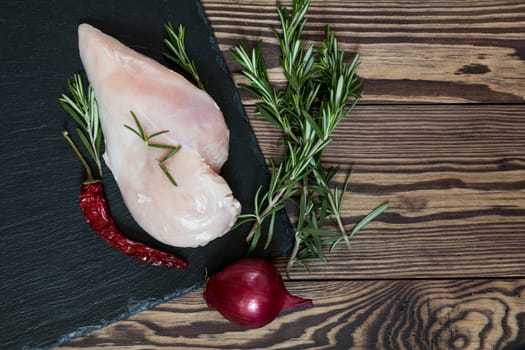 Raw uncooked chicken fillet on a cutting table with ingredients for cooking, on black stone board. Top view. Toned. Copy space.