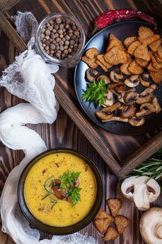 Pea soup with mushrooms in black plate. Fried mushrooms. Dried pea, pepper in glass jars.  Fresh parsley and rosemary. Rye crackers. Dark wooden table. Toned.