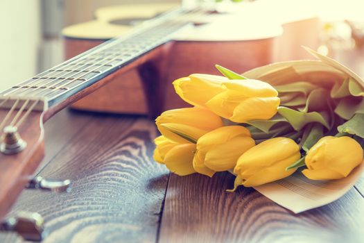 Beautiful spring background music. Guitar, yellow tulips, musical page on a dark wooden background. Shallow depth of field. Coloring and processing photo with soft focus in instagram style.