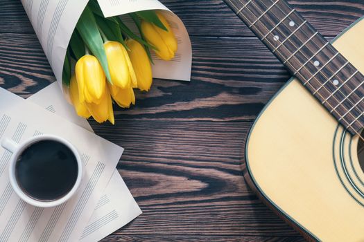 Beautiful spring background music. Guitar, yellow tulips, cup of coffee, musical page on a dark wooden background. Shallow depth of field. Coloring photo with soft focus in instagram style.