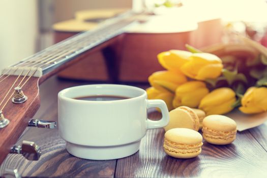 Beautiful spring music background. Cup of coffww, guitar, yellow tulips, musical page on a dark wooden background. Shallow depth of field. Coloring photo with soft focus in instagram style