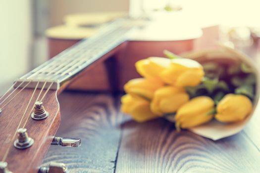 Beautiful spring background music. Guitar, yellow tulips, musical page on a dark wooden background. Shallow depth of field. Coloring and processing photo with soft focus in instagram style.