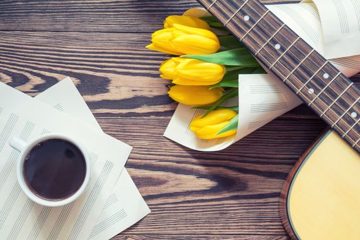 Beautiful spring background music. Guitar, yellow tulips, cup of coffee, musical page on a dark wooden background. Shallow depth of field. Coloring photo with soft focus in instagram style.