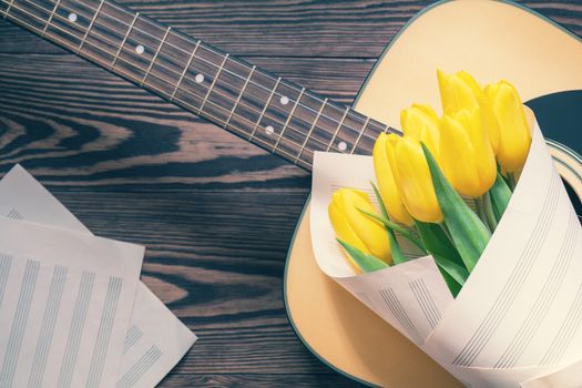 Beautiful spring background music. Guitar, yellow tulips, musical page on a dark wooden background. Shallow depth of field. Coloring and processing photo with soft focus in instagram style.