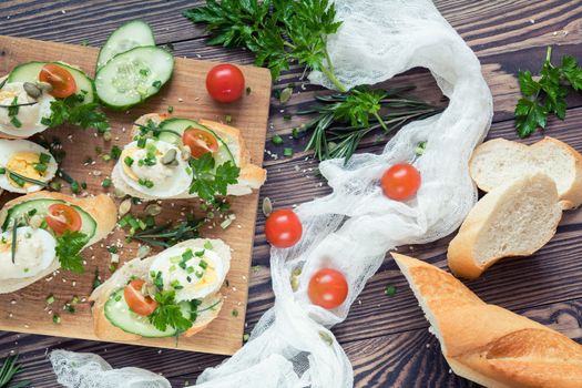 Bread with slices of fresh cucumber, egg, tomato and cream cheese on a wooden cutting board. Fresh parsley and rosemary.