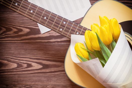 Beautiful spring background music. Guitar, yellow tulips, musical page on a dark wooden background. Shallow depth of field. Coloring and processing photo with soft focus in instagram style.