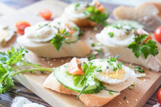 Bread with slices of fresh cucumber, egg, tomato and cream cheese on a wooden cutting board. Fresh parsley and rosemary.