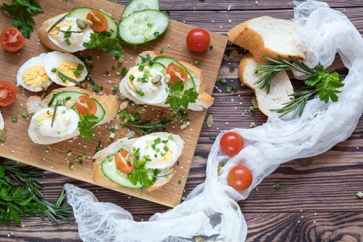 Bread with slices of fresh cucumber, egg, tomato and cream cheese on a wooden cutting board. Fresh parsley and rosemary.