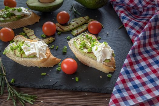 Bread with slices of grilled avocado and cream cheese on a black cutting stone board. Fresh parsley and rosemary. Vegetarian, vegan concept.