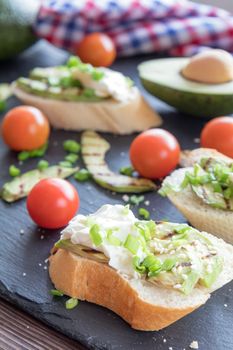 Bread with slices of grilled avocado and cream cheese on a black cutting stone board. Fresh parsley and rosemary. Vegetarian, vegan concept.