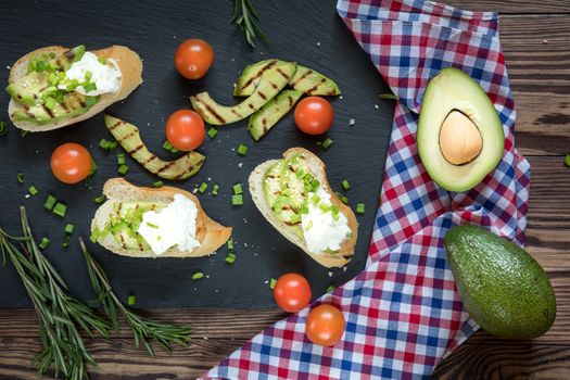 Bread with slices of grilled avocado and cream cheese on a black cutting stone board. Fresh parsley and rosemary. Vegetarian, vegan concept.