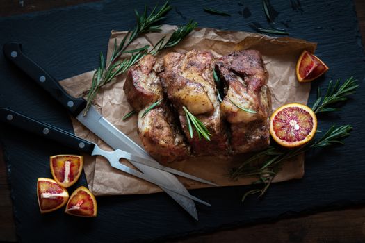 Sliced baked pork with herbs on a stone cutting board on wooden background.Grilled steak on a paper. Rosemary and sliced sicilian blood oranges  on a dark groundwork.