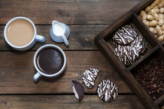 Cup of black coffee, cup of coffee with milk, cream. Marshmallow with chocolate, peanut and coffee beans in box. Dark wooden background. Beautiful vintage coffee groundwork. Coloring and processing photo.