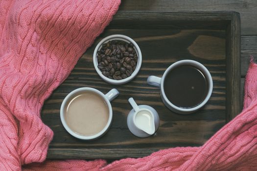 Cup of black coffee, cup of coffee with milk, cream and coffee beans in box. Dark wooden background. Pink woven scarf. Beautiful vintage coffee groundwork. Coloring and processing photo.