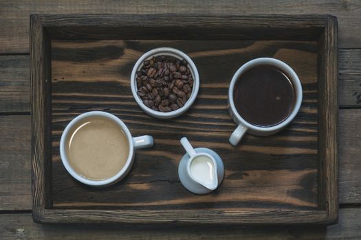 Cup of black coffee, cup of coffee with milk, cream and coffee beans in box. Dark wooden background. Beautiful vintage coffee groundwork. Coloring and processing photo.