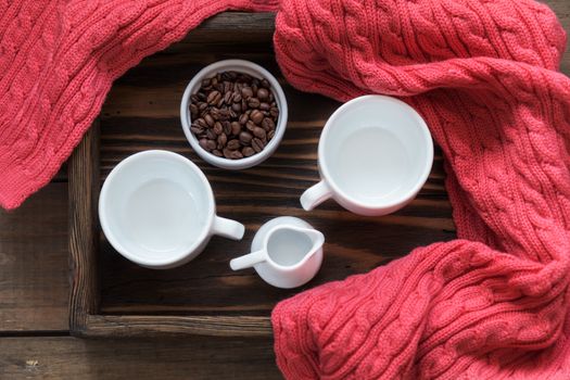 Two white cup, cream and coffee beans in box. Dark wooden background. Pink woven scarf. Beautiful vintage coffee groundwork. Coloring and processing photo.