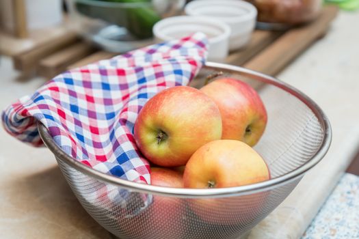 Raw fresh red apple with checkered napkin in sieve in a modern kitchen. Shallow depth of field. Toned.