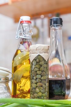 Caper in glass jar, balsamic vinegar and olive oil with pepper and spices in glass bottles in a modern kitchen. Shallow depth of field. Toned.