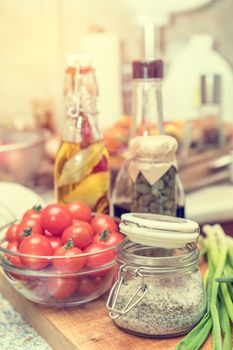 Salt with spices, caper in glass jar, balsamic vinegar and olive oil with pepper and spices in glass bottles, raw fresh cherry tomatoes in glass bowl in a modern kitchen. Shallow depth of field. Toned