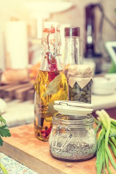 Salt with spices, caper in glass jar, balsamic vinegar and olive oil with pepper and spices in glass bottles in a modern kitchen. Shallow depth of field. Toned.