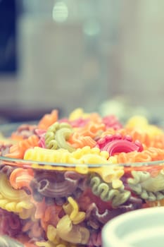 Raw multicolor creste di gallo pasta crude shells macaroni in glass bowl in a modern kitchen. Shallow depth of field. Toned