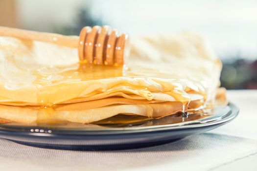 Honey is poured on a stack of pancakes. Sunlight. Close up.