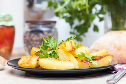 Delicious baked fried potatoes with parsley in black plate on table in the kitchen. Shallow depth of field. Coloring and processing photo.