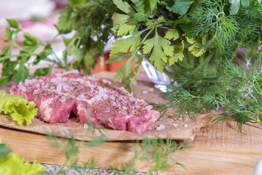 Fresh raw pork steak with salt and spices on paper. Fresh green dill and parsley.  Shallow depth of field. Coloring and processing photo.