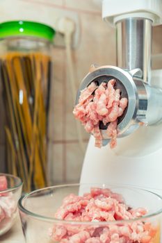 Home electric meat-grinder is making pork stuffing in a modern kitchen. Pork stuffing in a glass bowl.