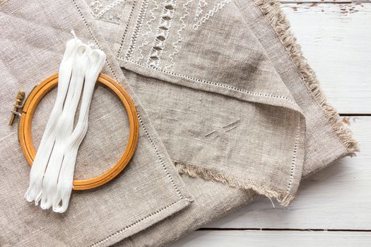 Set for embroidery. Embroidery thread white color, embroidery hoop and needle on linen with needlework in progress. Coloring and processing photos. Shallow depth of field.