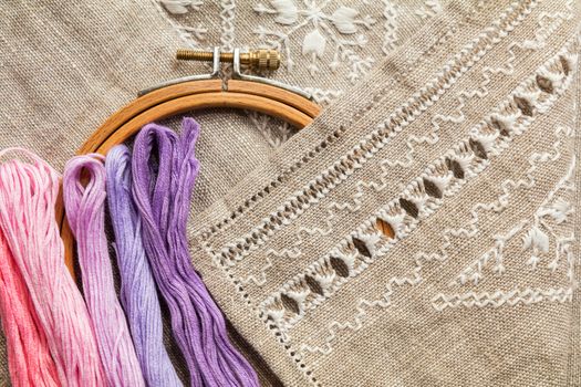 Set for embroidery. Embroidery thread shades of violet and pink color, embroidery hoop, scissors and needle on linen with needlework in progress. Coloring and processing photos Shallow depth of field.