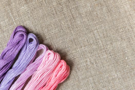 Set for embroidery. Embroidery thread shades of violet and pink color on linen homespun cloth. Coloring and processing photos. Shallow depth of field.