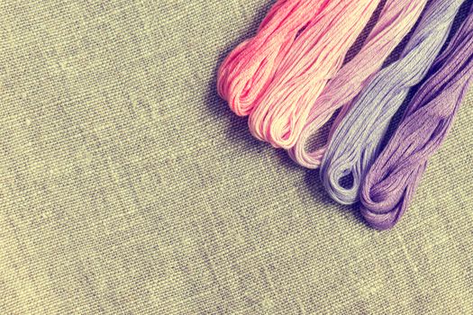 Set for embroidery. Embroidery thread shades of violet and pink color on linen homespun cloth. Coloring and processing photos. Shallow depth of field.