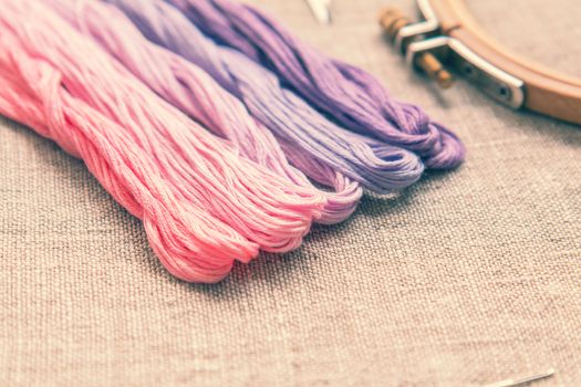 Set for embroidery. Embroidery thread shades of violet and pink color on linen homespun cloth. Coloring and processing photos. Shallow depth of field.