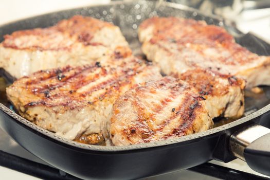 Fresh pork steak with spices cooking on teflon pan grill. Shallow depth of field.