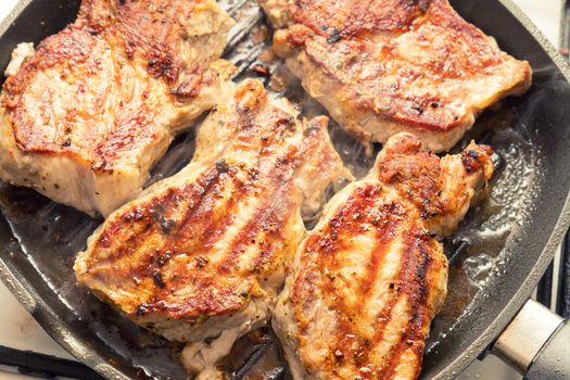 Fresh pork steak with spices cooking on teflon pan grill. Shallow depth of field.