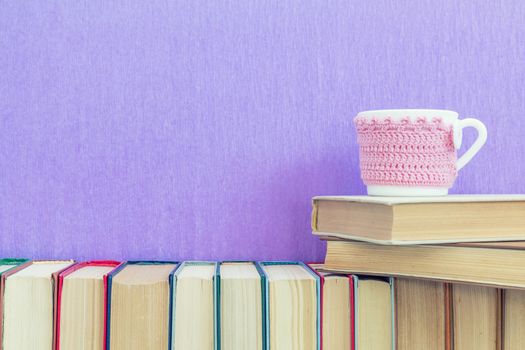 Books background. Many different books on violet wall. Cup of tea on books stack.