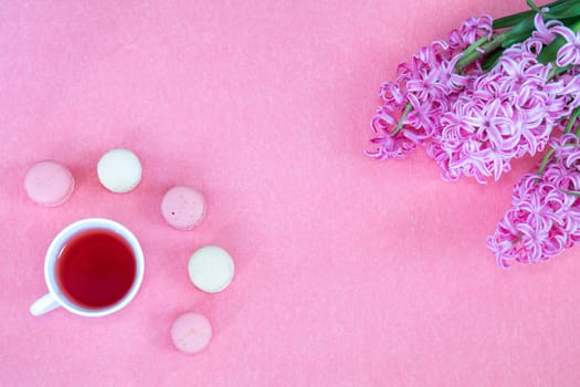 Beautiful spring holiday background. Cup of tea, fresh pink hyacinth and sweet  berry and vanilla macaroons cookies on pink copy space groundwork.