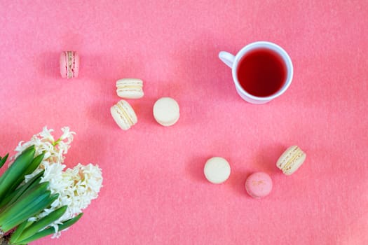 Beautiful spring holiday background. Cup of tea, fresh white hyacinth and sweet  berry and vanilla macaroons cookies on pink copy space groundwork.