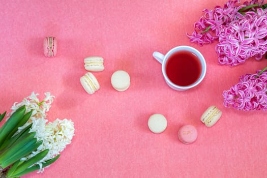 Beautiful spring holiday background. Cup of tea, fresh white and pink hyacinth and sweet  berry and vanilla macaroons cookies on pink copy space groundwork.