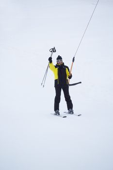 Happy smiling male skier using t bar ski drag lift and greeting waving his ski poles