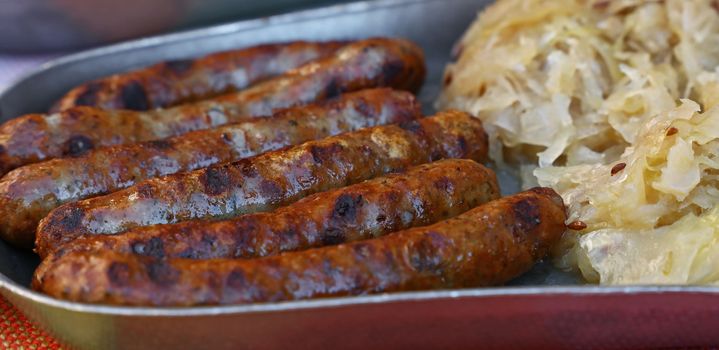 Close up portion of grilled Nuremberg Bratwurst sausages with side dish of sauerkraut on metal pewter plate, low angle view