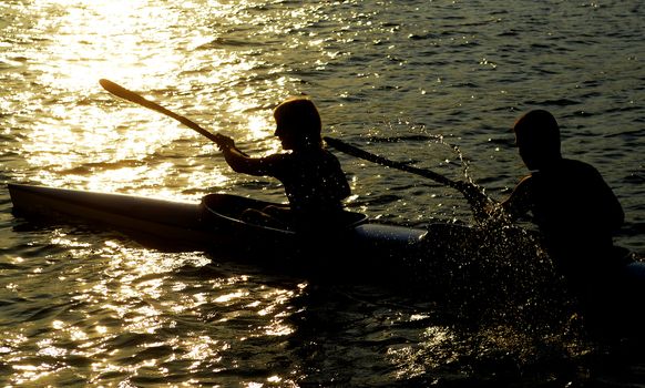 Young people rowing on the river at sunset